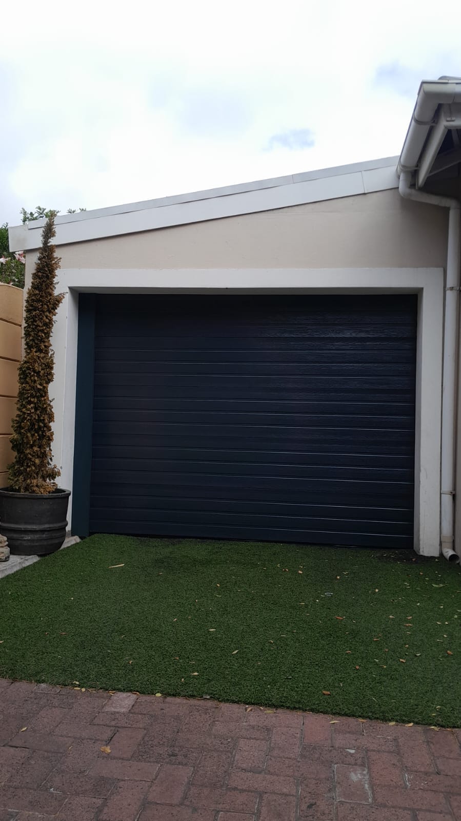 Charcoal sectional garage door beside artificial lawn