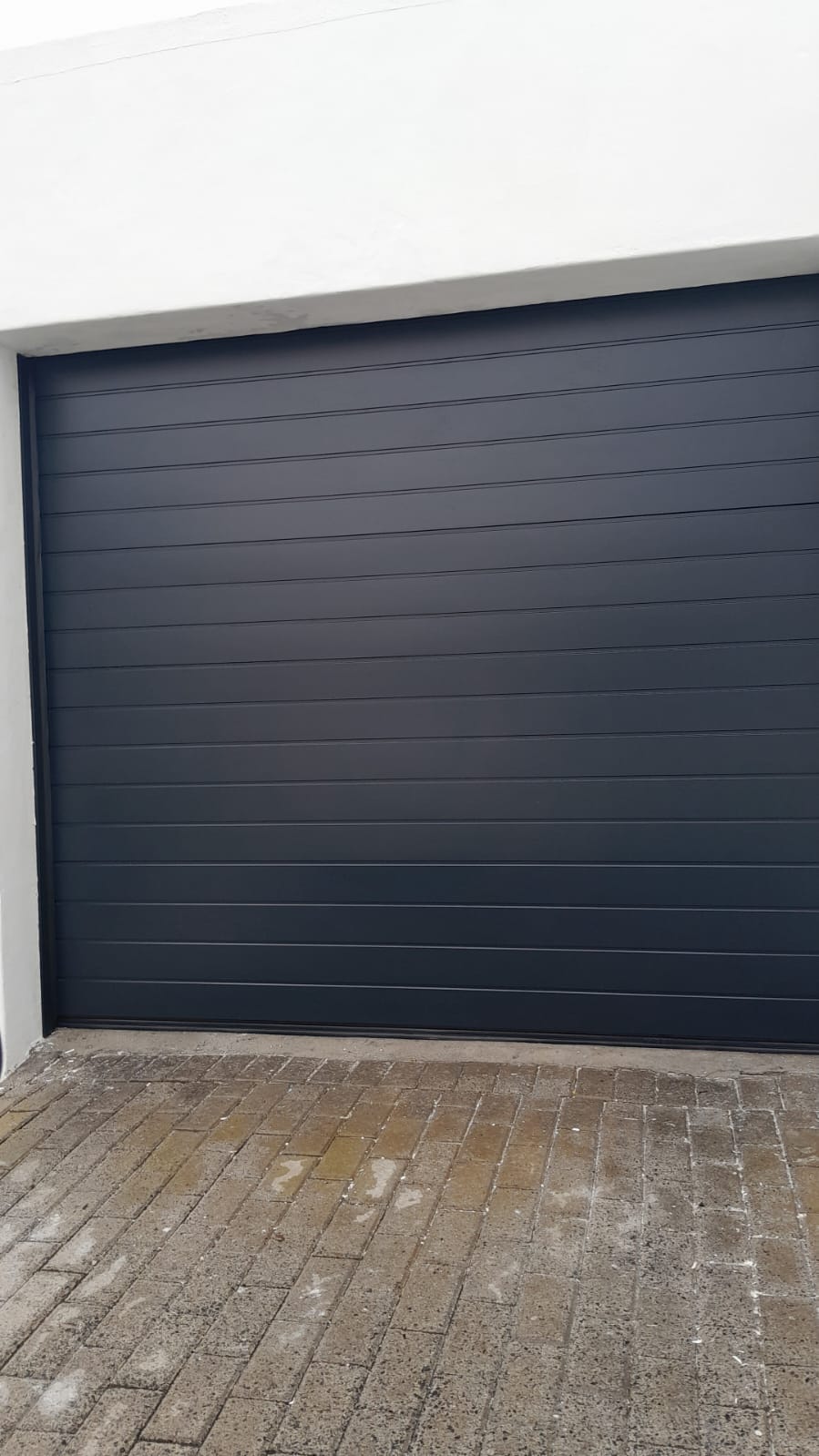 Charcoal sectional garage door above brick paving